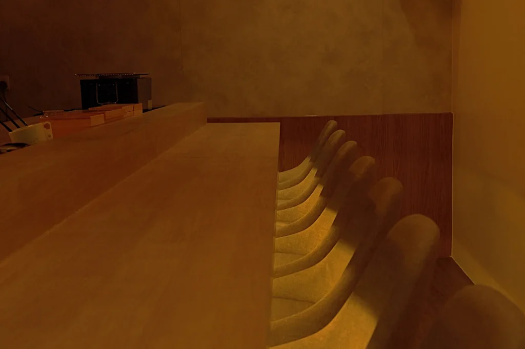 A dimly lit interior of a minimalistic omakase counter with several empty stools arranged in one line.