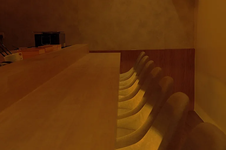 A dimly lit interior of a minimalistic omakase counter with several empty stools arranged in one line.