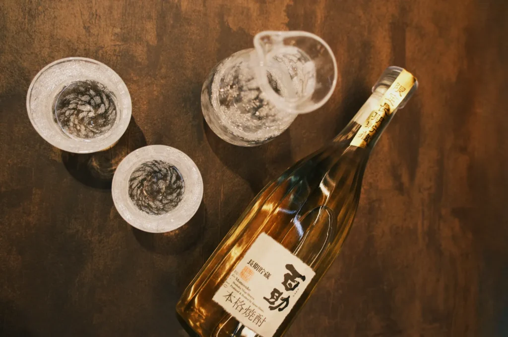 A bottle of alcoholic beverage with two glasses and a pitcher on a wooden surface.