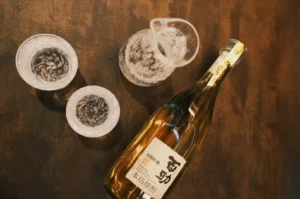 A bottle of alcoholic beverage with two glasses and a pitcher on a wooden surface.