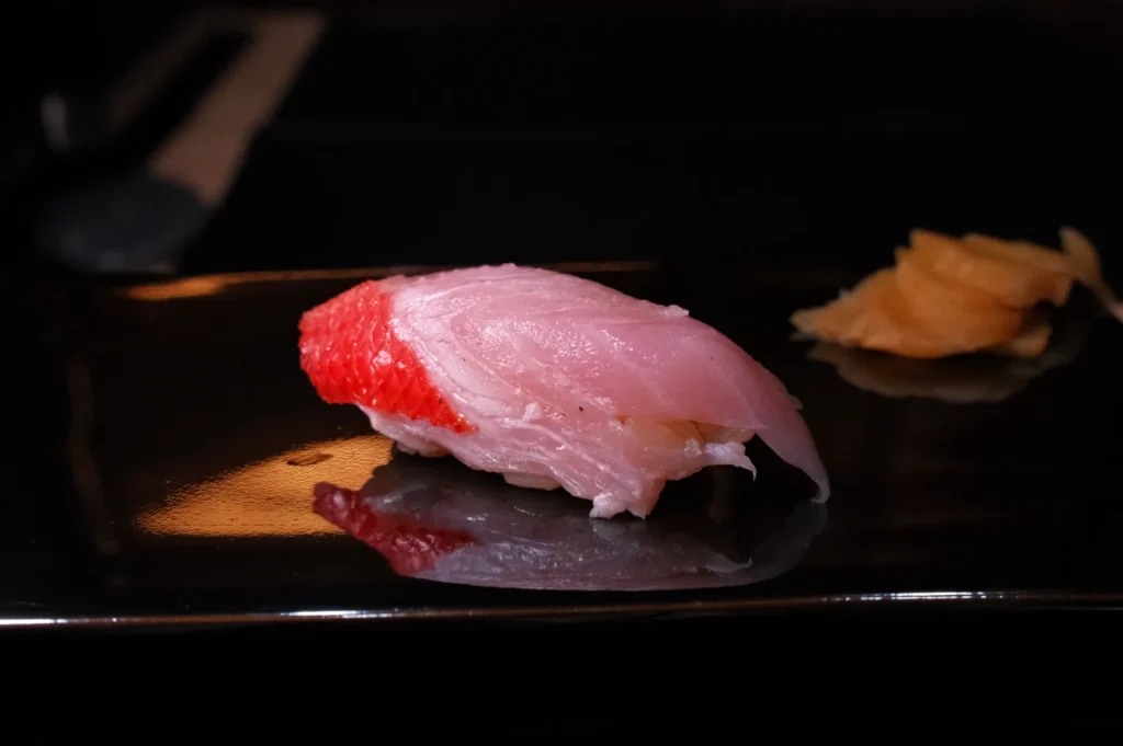 A piece of sushi on a black plate, featuring pink fish and a small portion of pickled ginger.