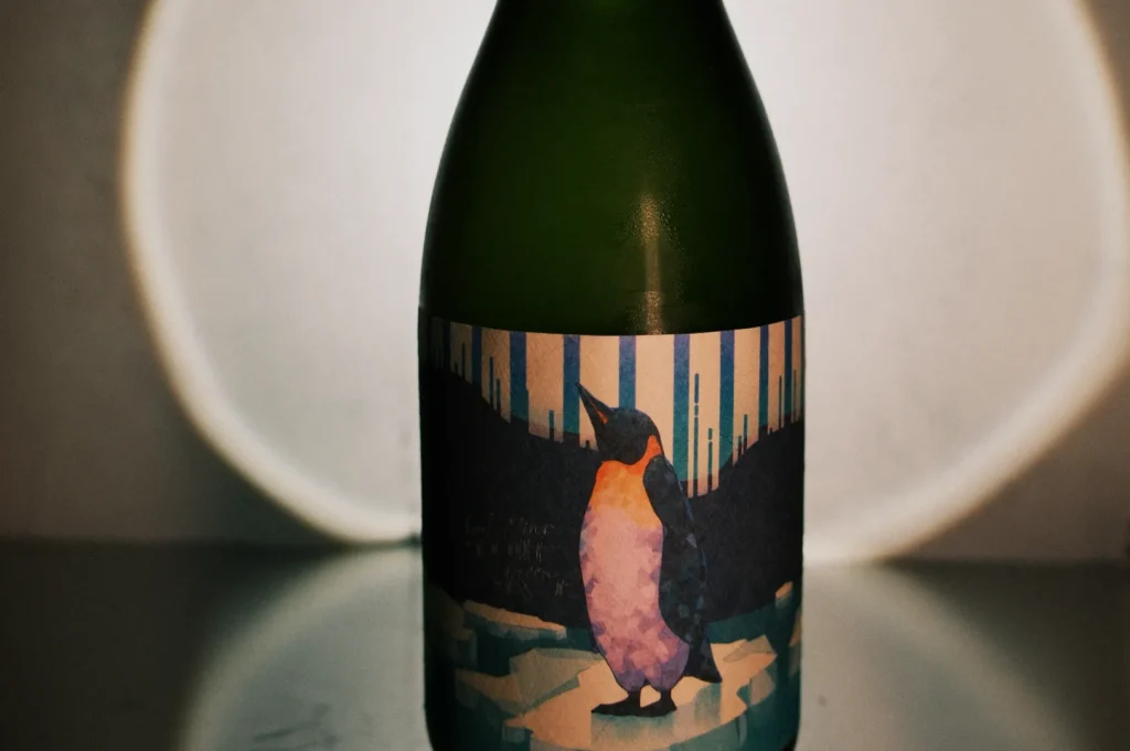 A bottle of sake featuring a penguin illustration on the label, set against a dimly lit background.