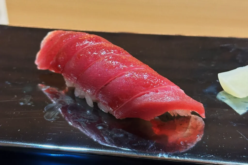 A piece of akami sushi with slices of tuna on top resting on a black plate.