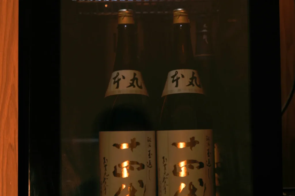 Two bottles of sake in a refrigerator, illuminated from behind.
