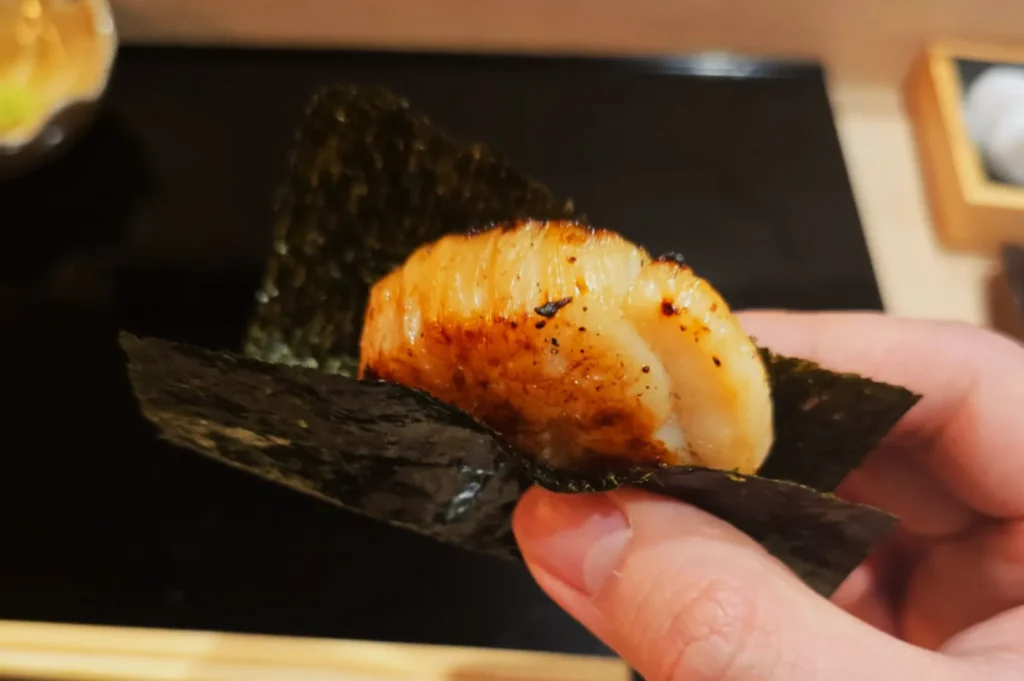 A hand holding a piece of sushi wrapped in nori in an omakase dinner.