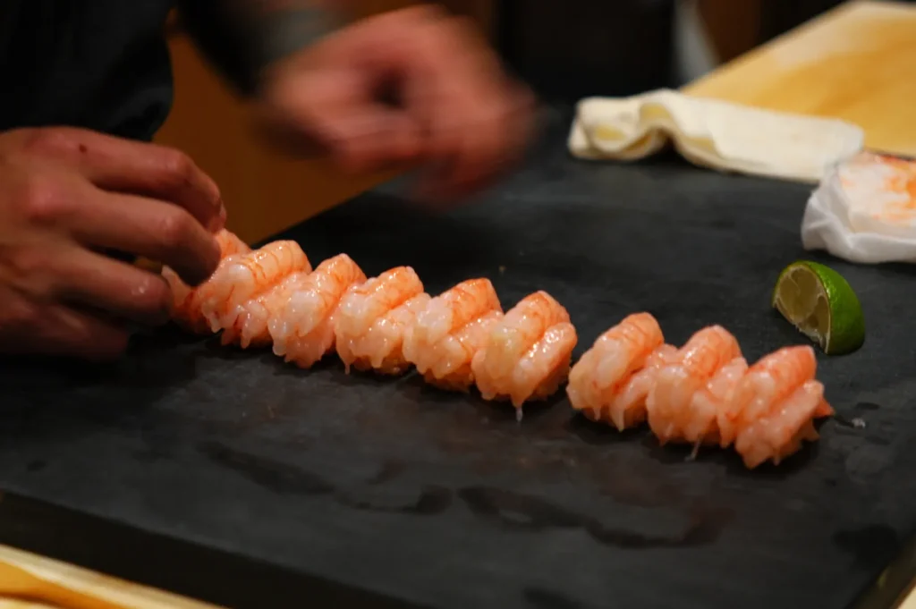 A chef preparing sushi on a black slate surface, featuring neatly arranged pieces of sushi with a lime wedge nearby.