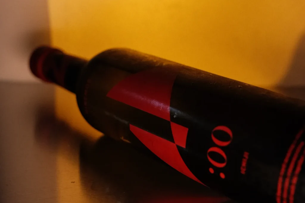A bottle of wine with a black label featuring a bold red design, lying on its side against an orange background.