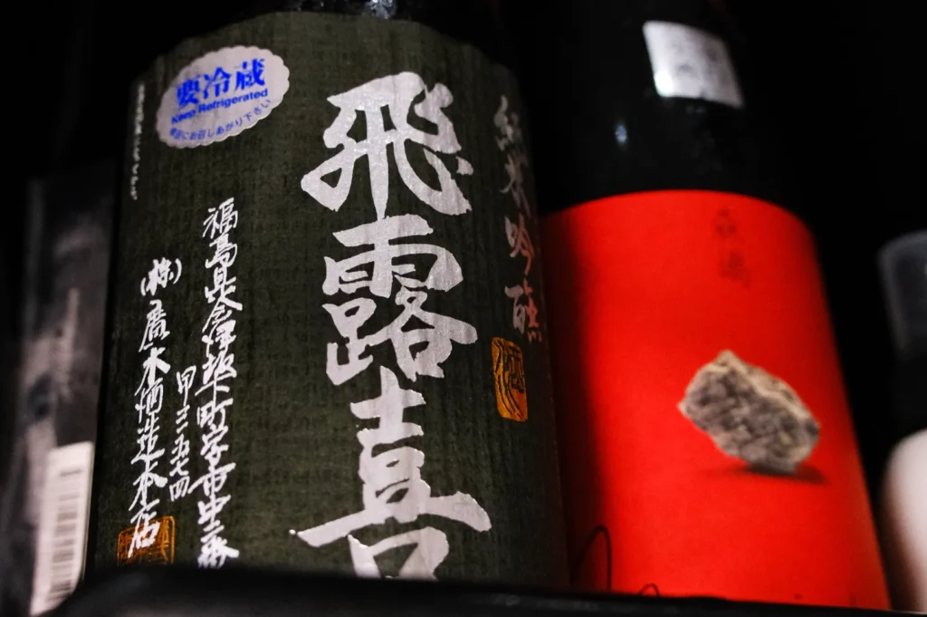 A close-up of a bottle of sake on a shelf, featuring decorative Japanese characters and symbols on the label.