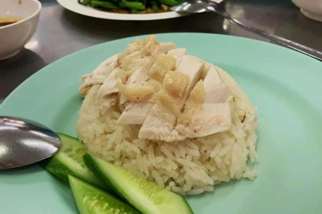 Hainanese chicken rice served on a light blue plate with sliced cucumber. The dish appears fresh and simple, evoking a sense of comfort.