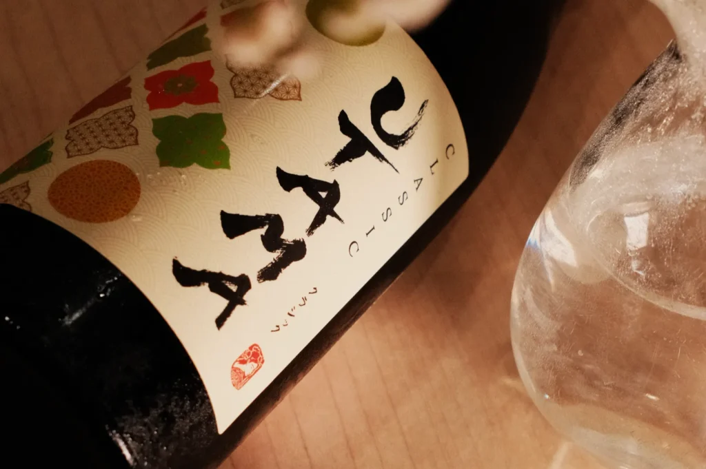 A close-up of a wine bottle with a stylized label featuring colorful designs and characters, next to a glass.