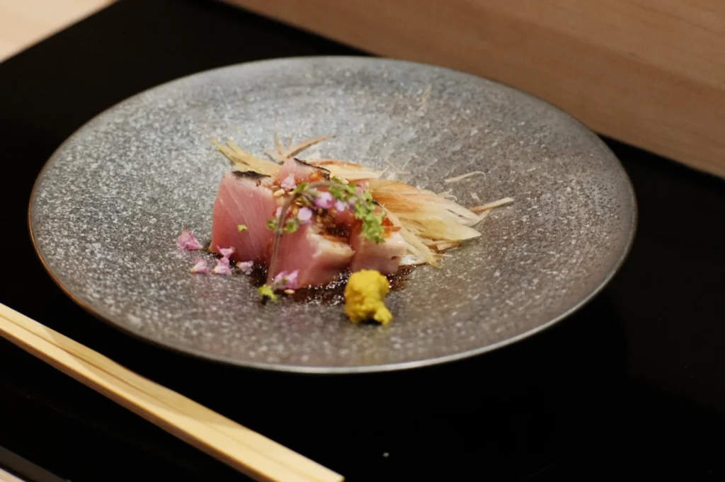 A plate of sushi featuring a piece of fish garnished with herbs and sauces, served with chopsticks on the side.