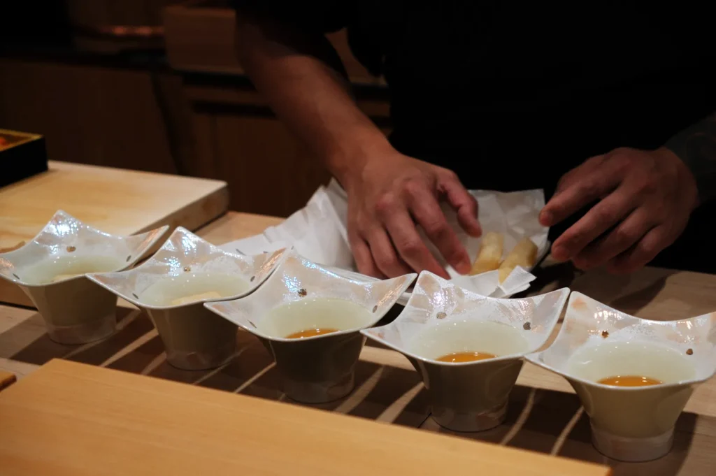 A person’s hands preparing food with multiple small bowls arranged in a line on a countertop.