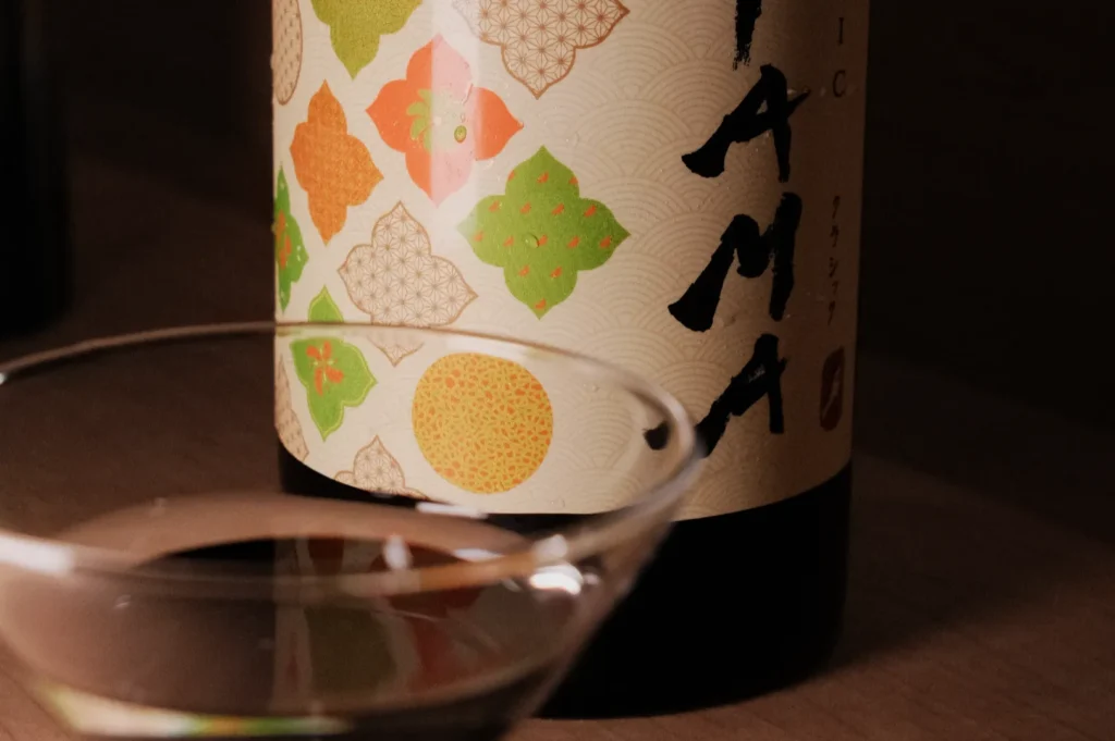 A close-up of a wine bottle with a decorative label featuring colorful patterns and a glass in the foreground containing a clear liquid.