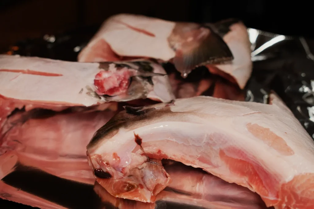 Raw fish heads and body sections on aluminum foil, showcasing pink flesh and gray skin. The scene suggests preparation for cooking.