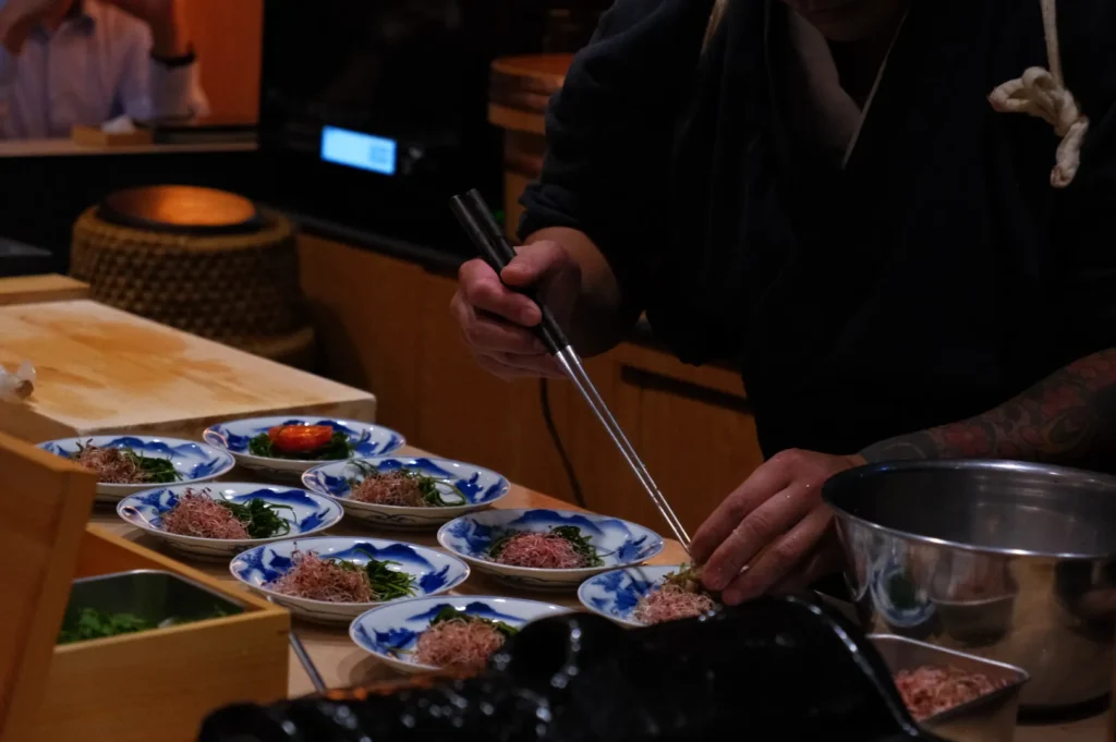 Chef Masa using chopsticks to arrange food on plates in a culinary setting.
