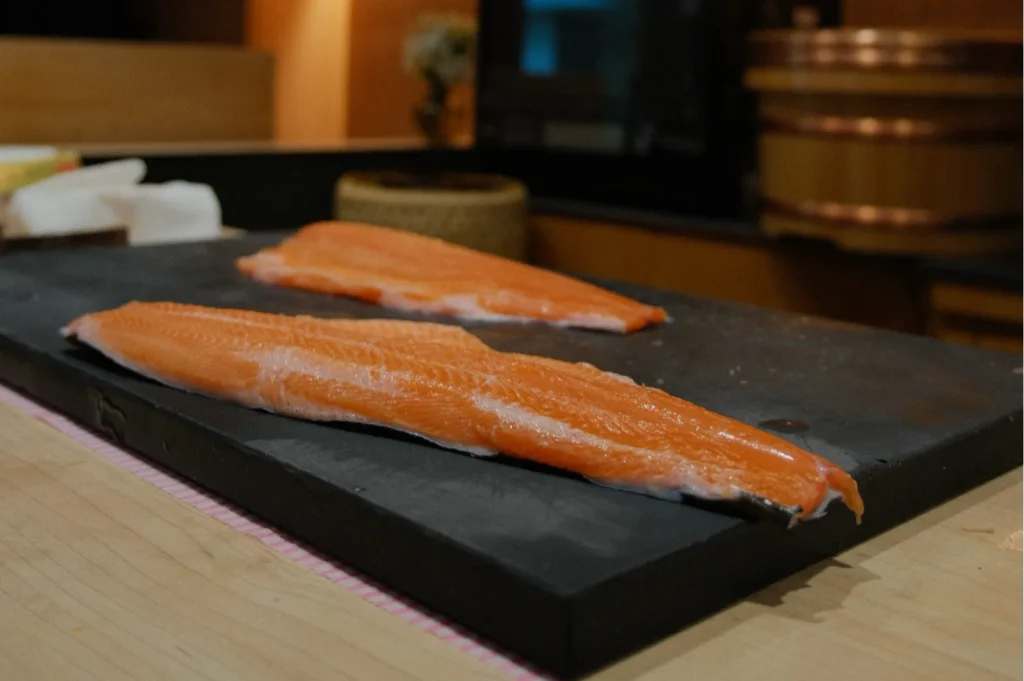 Two fillets of fresh salmon on a black cutting board.