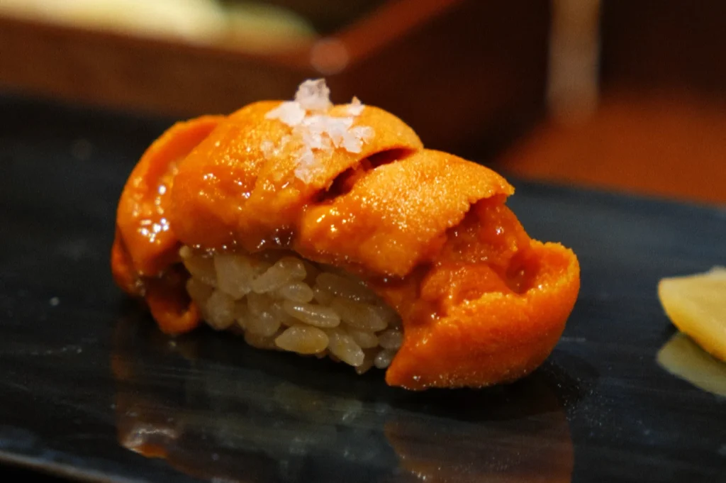 A piece of sushi featuring sea urchin (uni) on top of vinegared rice, garnished with a sprinkle of sea salt.