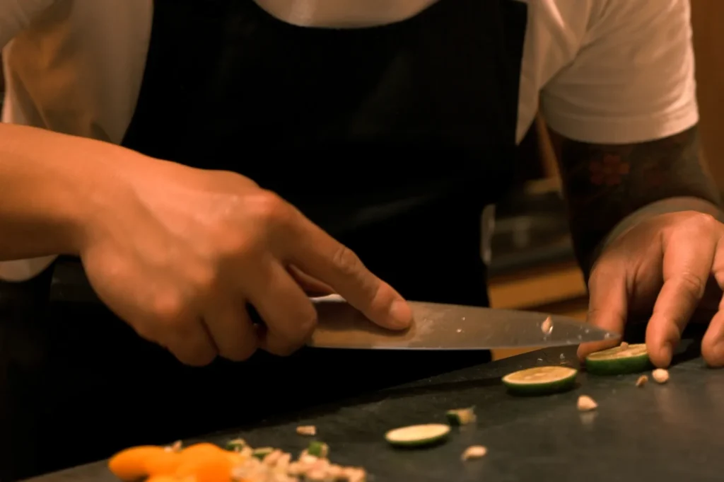 Chef Masa in a black apron slicing lime on a black cutting board.