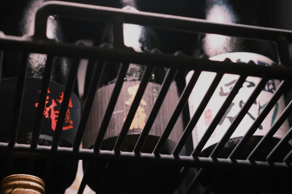 Three bottles on a rack, partially obscured by metal bars, displaying various designs and labels.