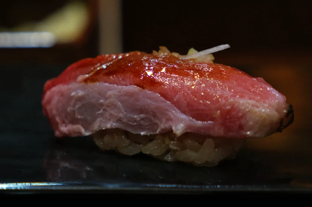 A piece of sushi topped with a slice of red, marbled fish, resting on a small mound of rice.