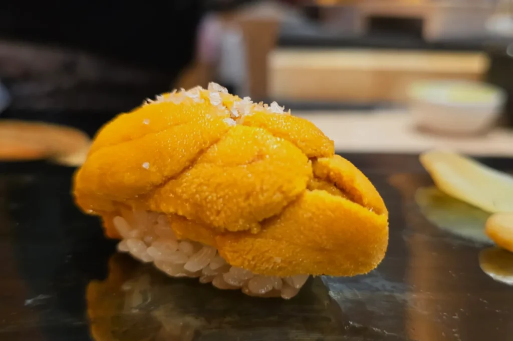 A piece of sushi topped with bright orange sea urchin (uni) on a small bed of rice.