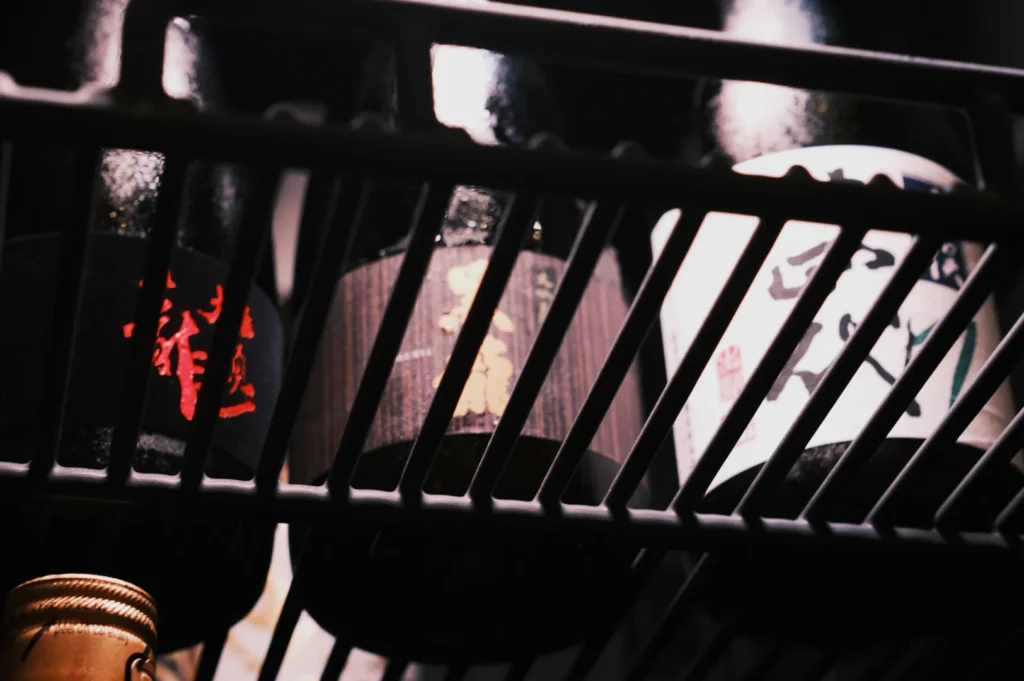 A close-up of several bottles of sake stored on a fridge shelf, with labels in Japanese characters.