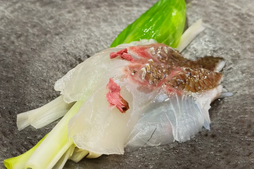 Close-up of a piece of madai sushi placed on a bed of green onion leaves.