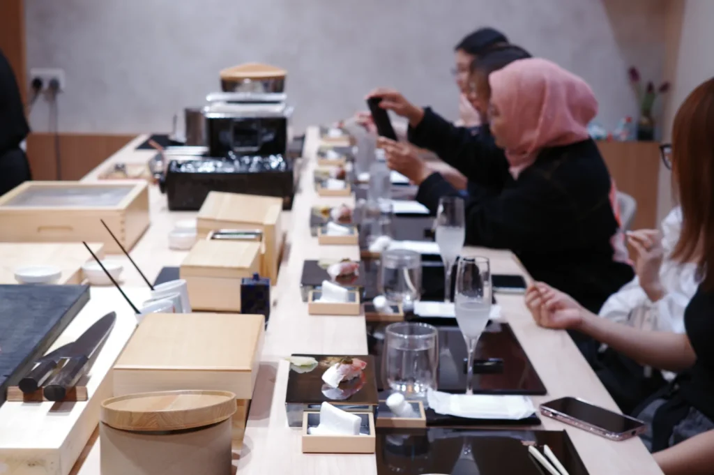 A group of people seated at a sushi restaurant, with sushi plates and dining utensils laid out in front of them.