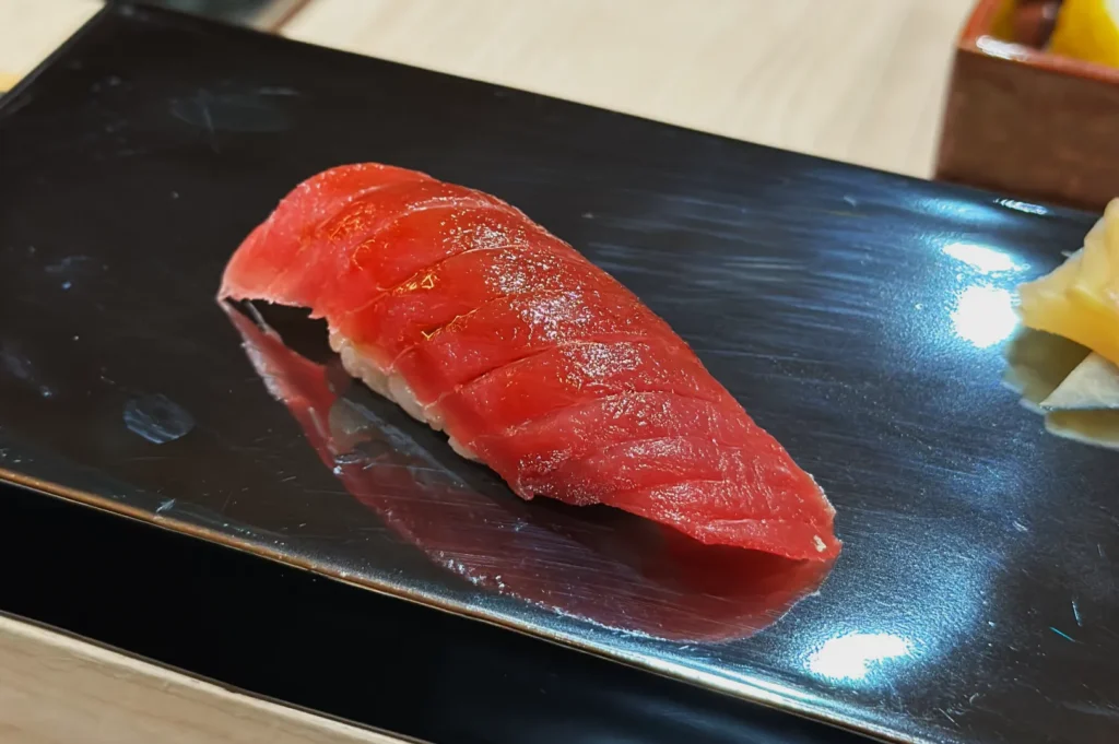 A piece of akami sushi with a slice of red fish on top, placed on a black rectangular plate.