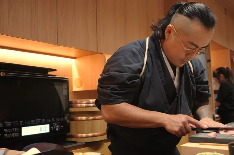 A chef working diligently in a kitchen, preparing sushi with a focused expression while wearing a traditional Japanese robe.
