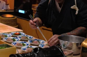 A chef carefully plating food on traditional Japanese dishes in a restaurant setting.
