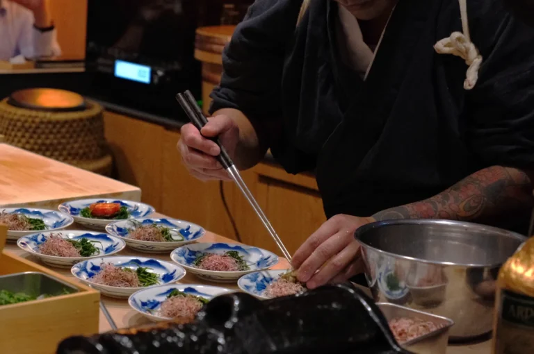 A chef carefully plating food on traditional Japanese dishes in a restaurant setting.