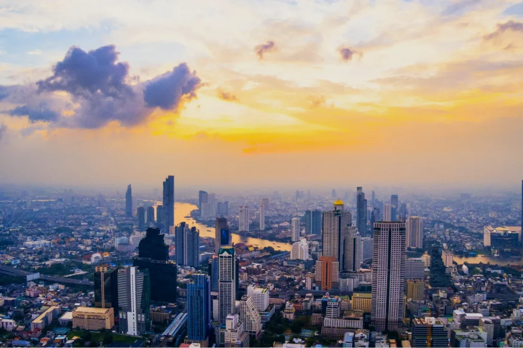 Aerial view of a bustling city skyline at sunset, with high-rise buildings and a river reflecting the colorful sky.