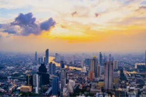 Aerial view of a bustling city skyline at sunset, with high-rise buildings and a river reflecting the colorful sky.