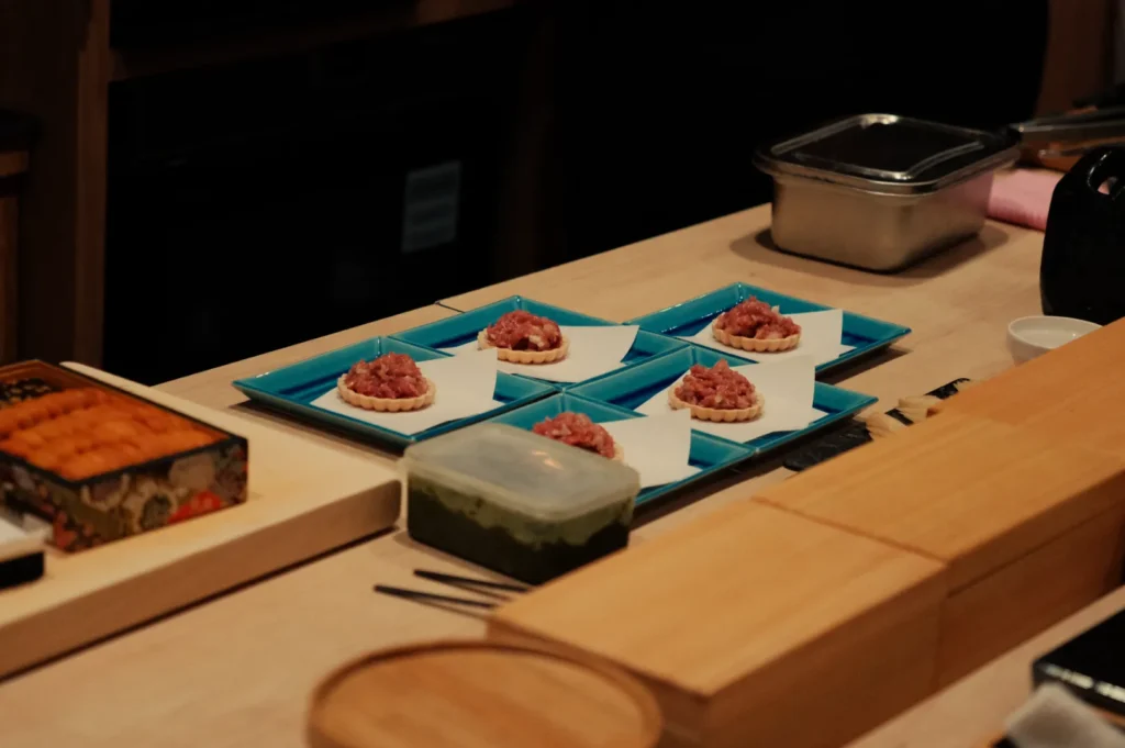 A wooden table with several plates arranged on it, each holding small portions of food, alongside containers of ingredients and utensils.