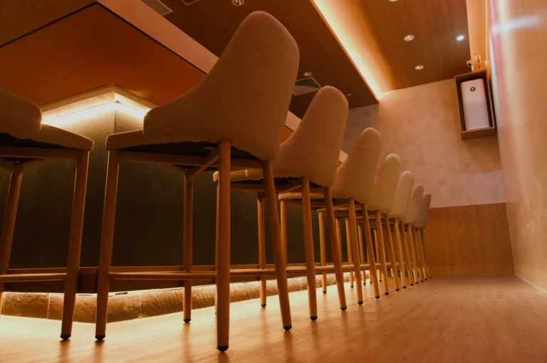 A row of empty, high-backed chairs with wooden legs against a softly lit wall in a modern interior space.
