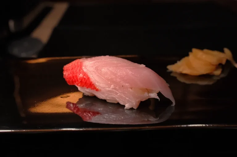 A piece of sushi on a dark plate, with a small mound of pickled ginger beside it.