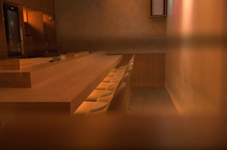 A minimalist restaurant interior featuring a wooden bar and seating, with warm lighting and a soft, muted atmosphere.