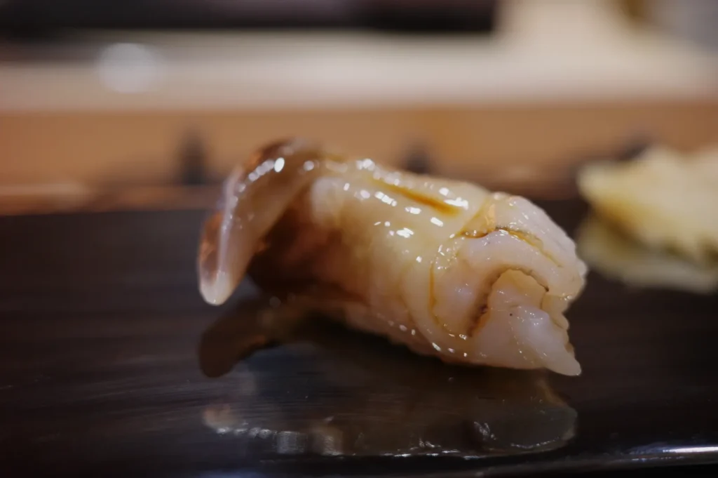 A piece of sushi with glistening seafood on a dark plate.