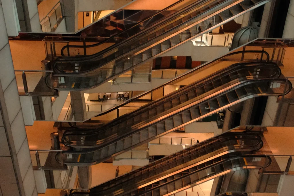 Escalators in a modern building, reflecting overhead lights and interior structures.