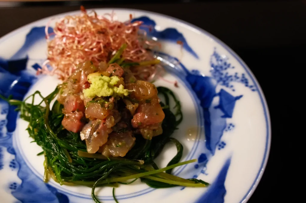 A plate with a mound of seaweed topped with diced raw fish and wasabi, garnished with a pile of shredded radish.