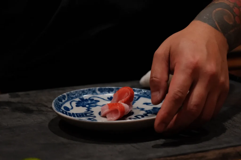 A hand placing a piece of sushi on a blue and white patterned plate.