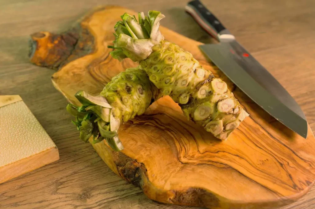 Two pieces of fresh wasabi root on a wooden cutting board, with a knife in the background.