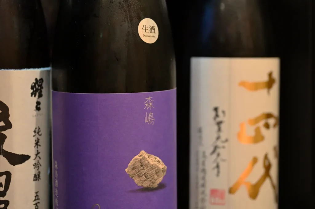 Three bottles of sake, with one prominently featuring a purple label with a rock graphic.