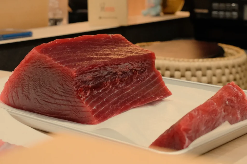 A large piece of red tuna on a white tray, with a smaller piece cut off beside it.