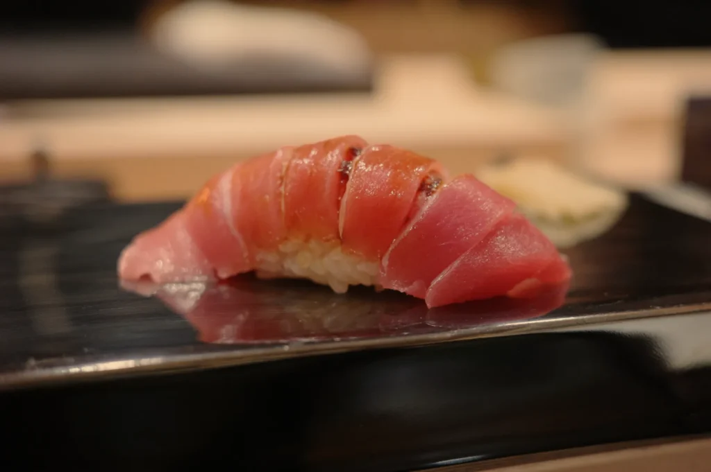 A piece of sushi featuring sliced tuna on top of vinegared rice, presented on a black plate.