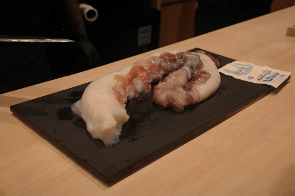 Sliced octopus placed on a black serving platter, with visible texture and color variations in the flesh.