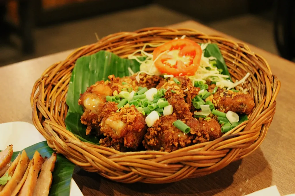A woven basket containing fried chicken drumsticks garnished with green onions, lettuce, and a slice of tomat