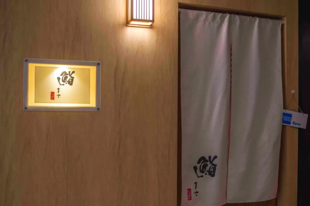 A wooden wall with a lit sign displaying a logo and a doorway covered by a fabric curtain.