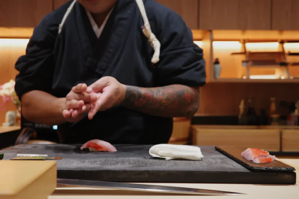 Chef Masa in a traditional black Japanese uniform, skillfully preparing sushi in a restaurant kitchen.